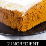 A slice of pumpkin spice cake with white frosting is displayed on a black plate. The text below the image reads "2 Ingredient Pumpkin Spice Cake.