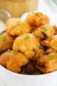 A bowl of golden-brown Air Fryer Cauliflower Wings, garnished with chopped green onions.
