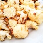A plate of air fryer fried cauliflower florets on a white dish, showing slightly browned edges.