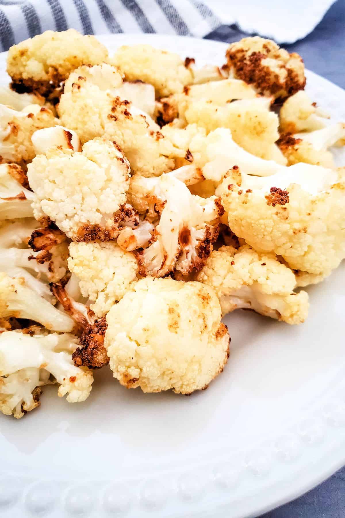 A plate of air fryer fried cauliflower florets on a white dish, showing slightly browned edges.