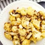 A white plate with florets, set on a gray surface with a striped cloth and garlic visible in the background.