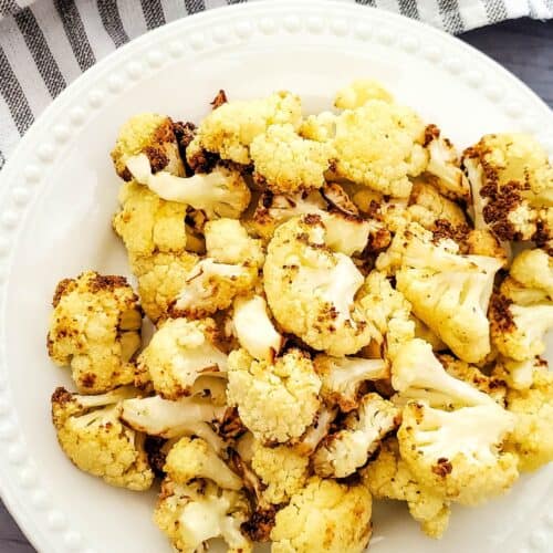 A white plate with florets, set on a gray surface with a striped cloth and garlic visible in the background.