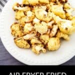 A white plate filled with crispy air fryer fried cauliflower sits on a gray surface next to a striped cloth.