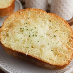 A slice of toasted Air Fryer Garlic Bread topped with melted cheese and sprinkled with herbs, served on a white plate.
