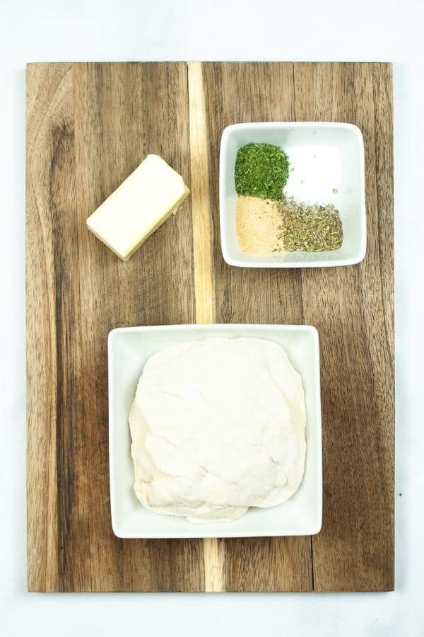 White plate with dough, seasoning and butter on wooden cutting board