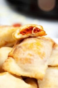 A close-up of a pile of air fryer pizza rolls, with one roll bitten to reveal its filling of tomato sauce and pepperoni.