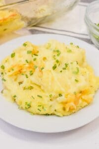 A serving of cheesy Baked Twice Mashed Potatoes topped with chopped chives is presented on a white plate for a comforting, savory dish.