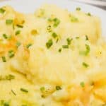 A serving of Baked Twice Mashed Potatoes mixed with cheese and topped with chopped chives on a white plate.