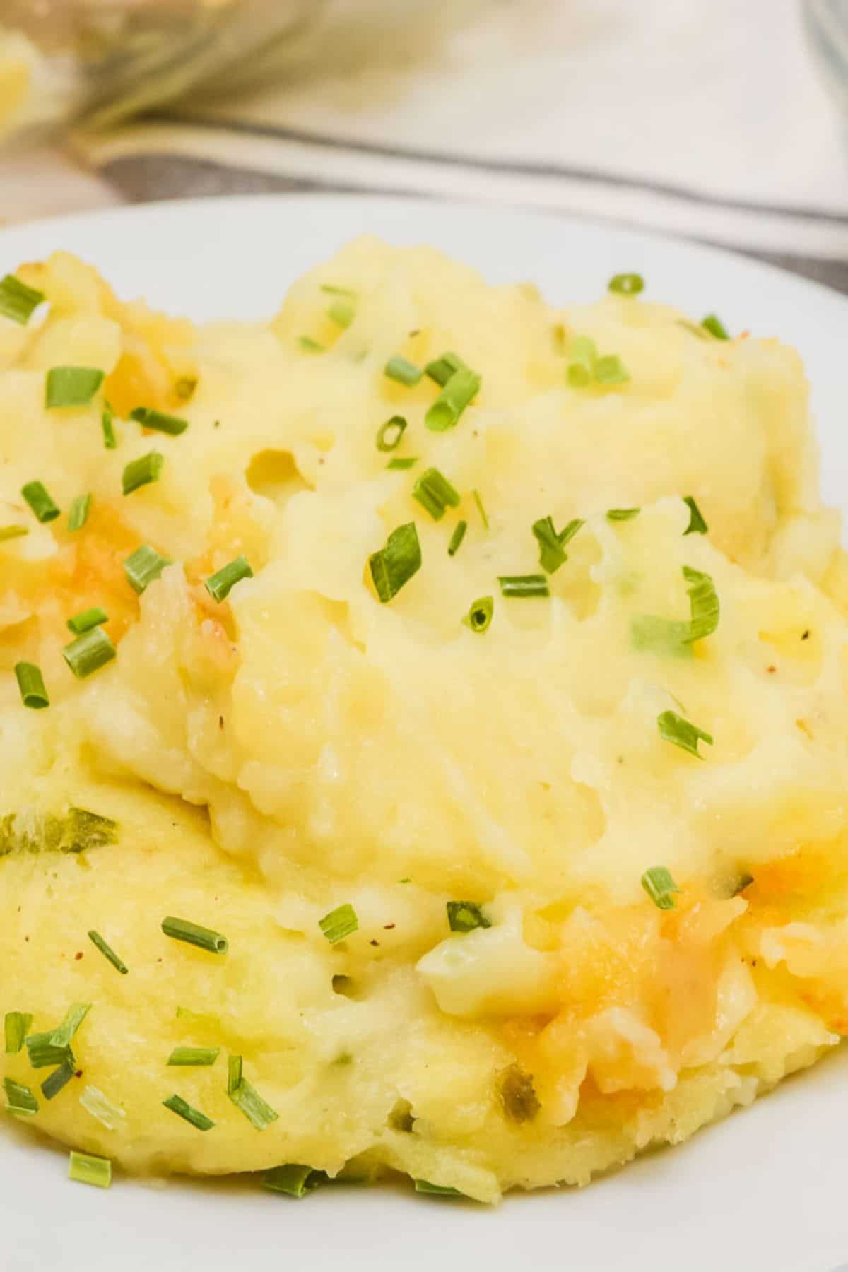 A serving of Baked Twice Mashed Potatoes mixed with cheese and topped with chopped chives on a white plate.