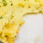 A glass baking dish containing casserole, topped with mashed potatoes and garnished with chopped chives; a portion has been removed.