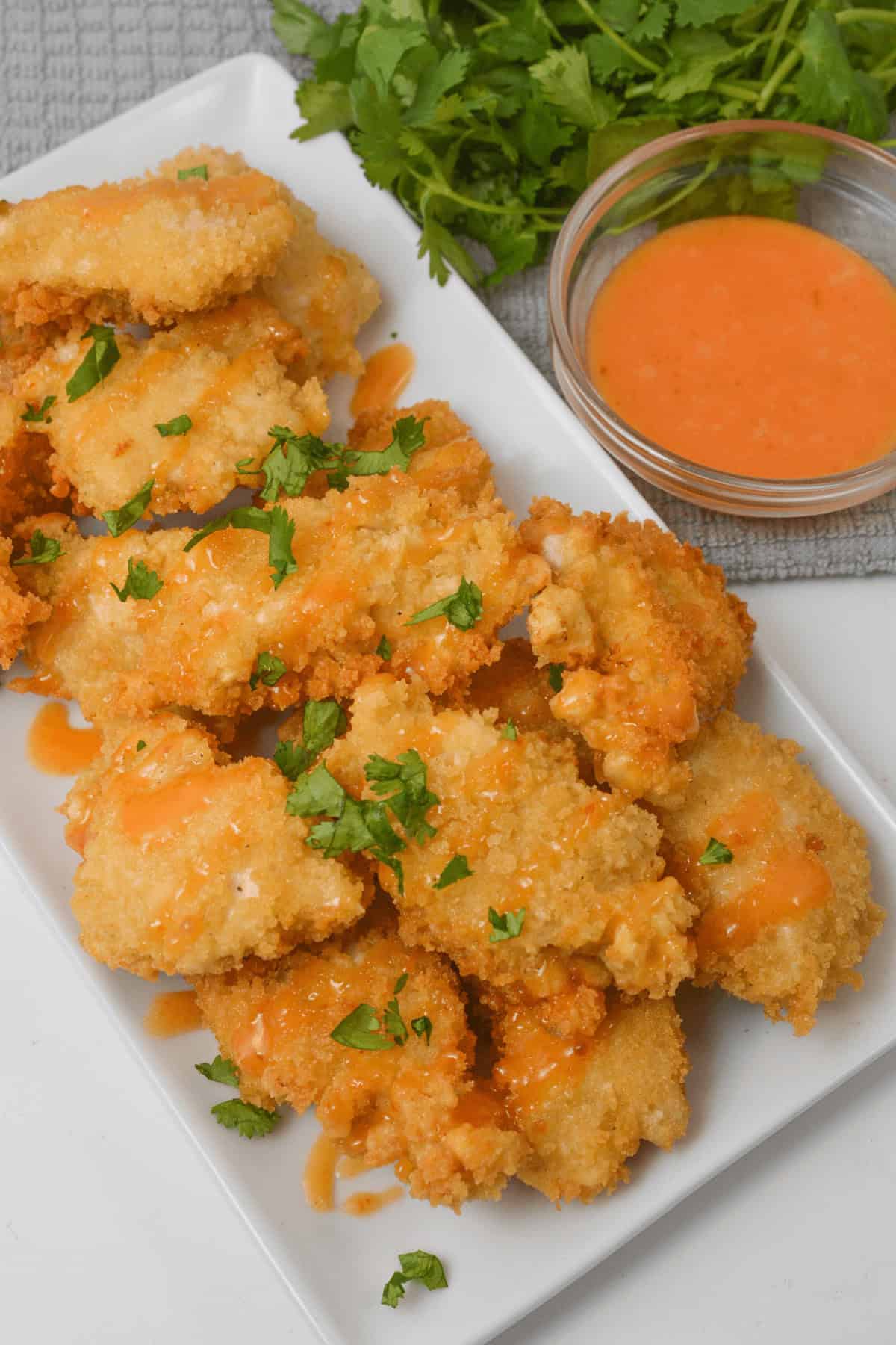 A plate of crispy bites garnished with chopped herbs, served with a small bowl of orange dipping sauce, and parsley in the background.