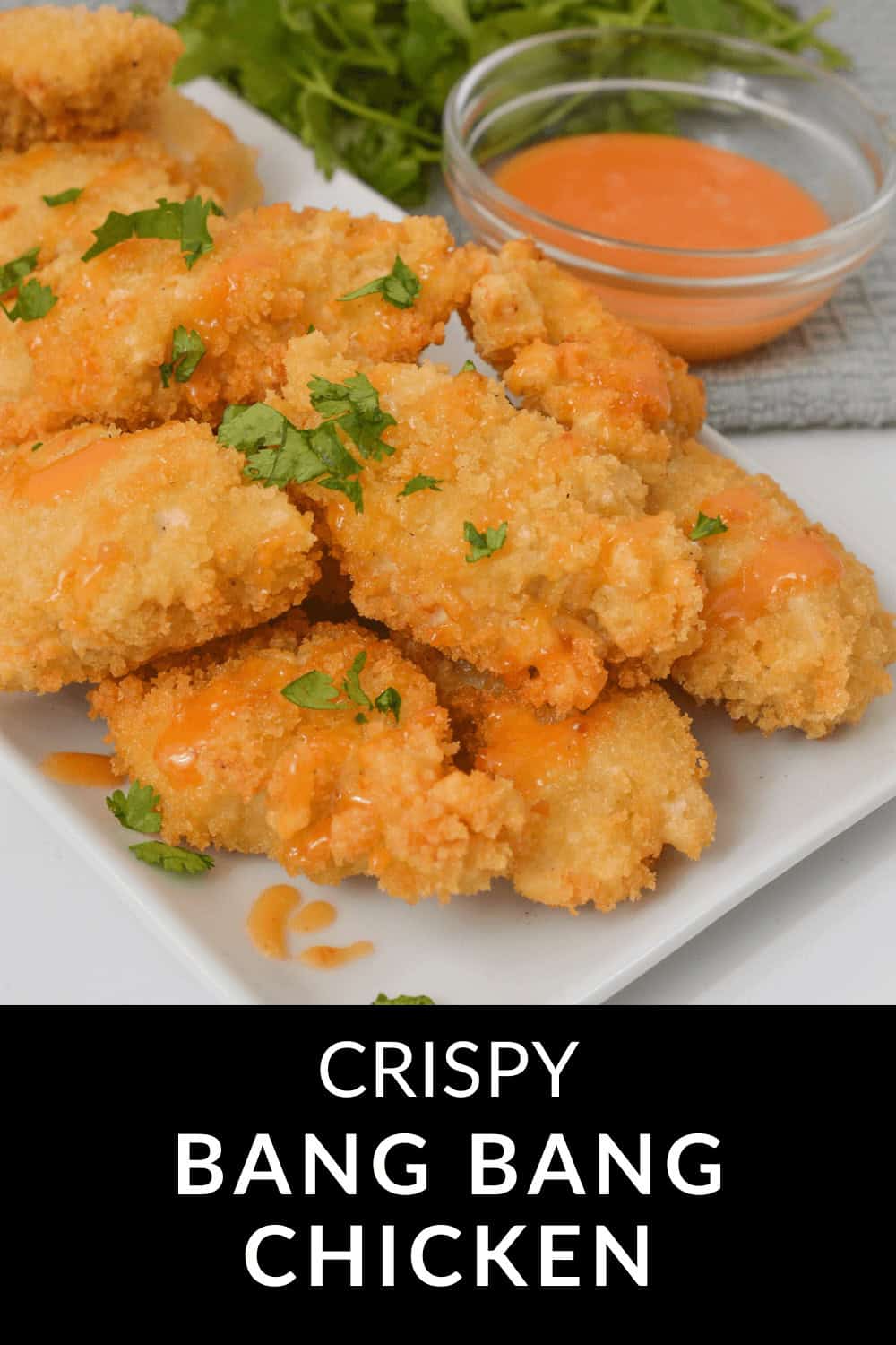 A plate of crispy Bang Bang Chicken garnished with parsley, served alongside a bowl of zesty orange sauce.