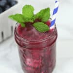 A drink topped with mints with a straw in it.