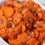 A white dish filled with brown sugar carrots and crispy bacon bits.