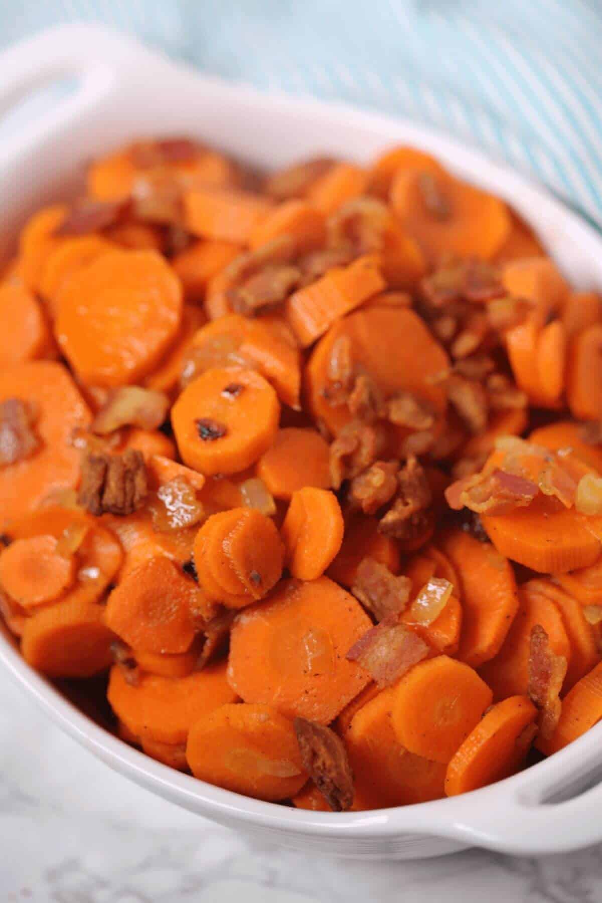 A white dish filled with brown sugar carrots and crispy bacon bits.