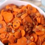 A white dish filled with brown sugar carrots and pecans creates a delightful harmony of flavors. A silver spoon rests in the background, ready to serve.