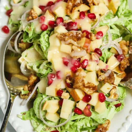 Brussels Sprouts Shaved Salad with shredded greens, diced apples, walnuts, pomegranate seeds, and creamy dressing on a white plate with a spoon.