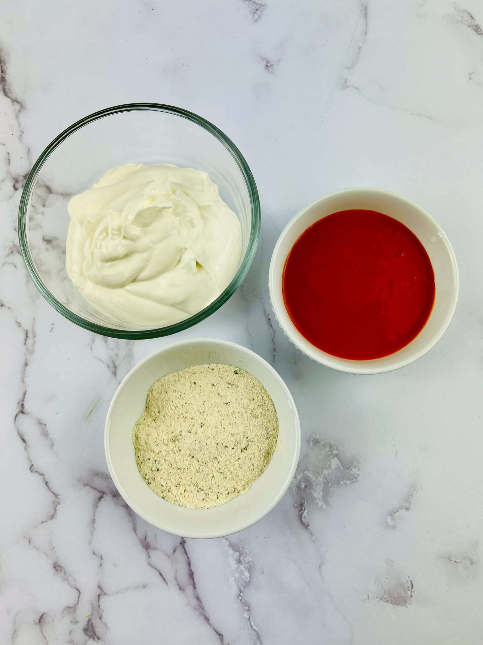 A bowl of ranch, a bowl of hot sauce, and seasoning.