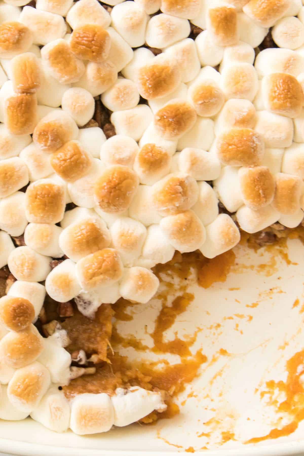 A casserole dish filled w with canned sweet potatoes, topped with toasted marshmallows, with a portion already served.