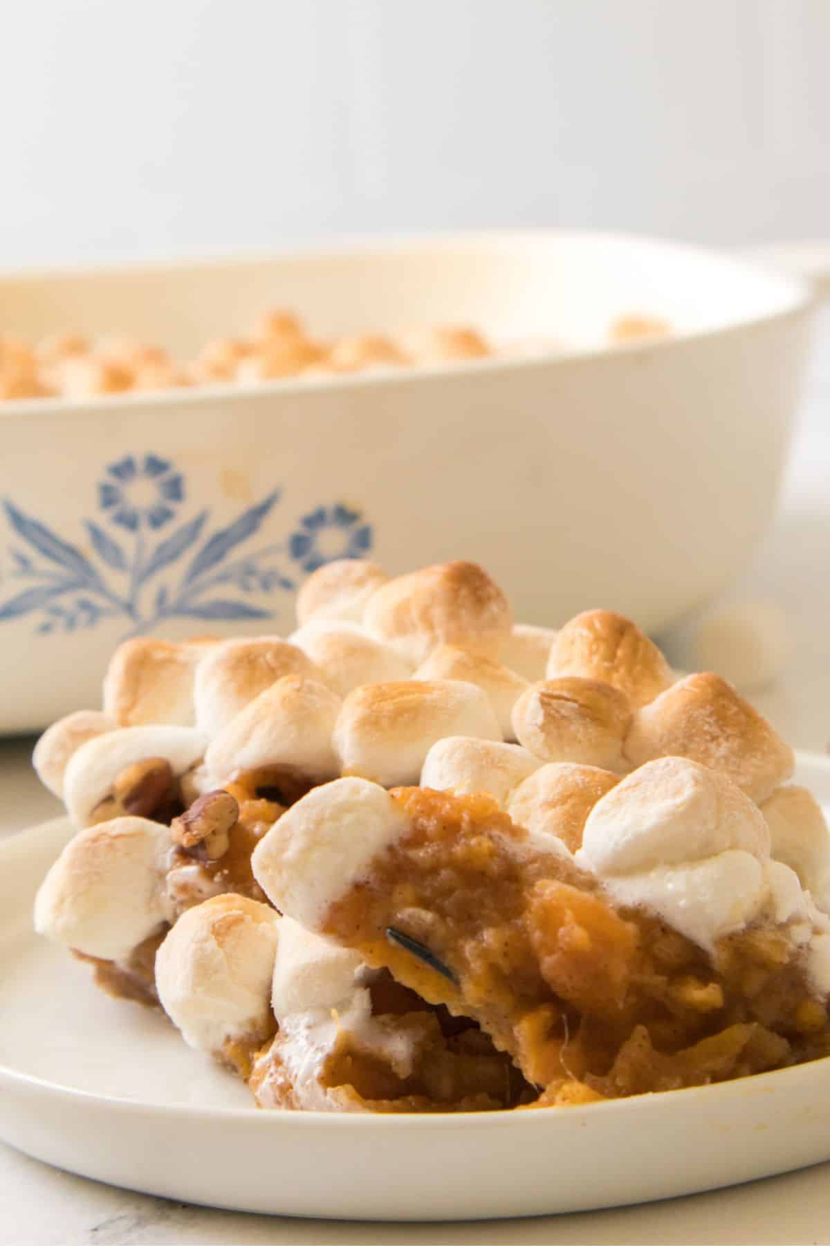 A serving of the dish topped with toasted marshmallows on a plate, with a casserole dish in the background.