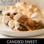 A serving of Candied Sweet Potatoes with Canned Sweet Potatoes topped with toasted marshmallows sits on a white plate, with a casserole dish in the background.