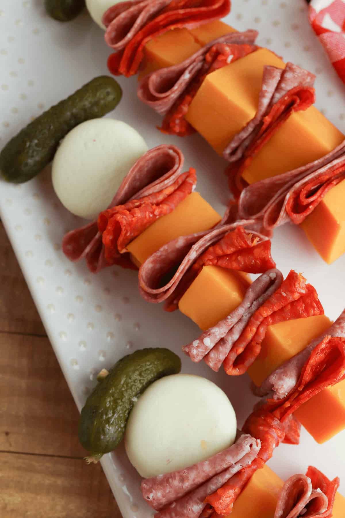 An arrangement of charcuterie skewers with cubes of cheese, slices of salami, pepperoni, boiled eggs, and pickles on a white tray.