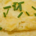 A bowl of cheesy mashed potatoes topped with chopped chives.