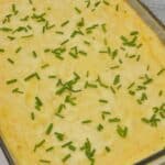 Casserole topped with chopped chives in a glass dish, resting on a gray textured cloth.