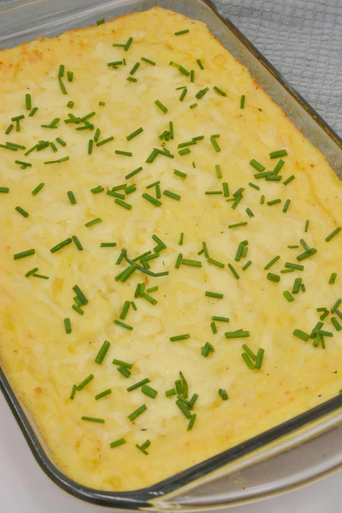Casserole topped with chopped chives in a glass dish, resting on a gray textured cloth.
