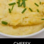 A bowl of creamy Cheesy Mashed Potatoes is topped with chopped chives, with the label "Cheesy Mashed Potatoes" at the bottom.