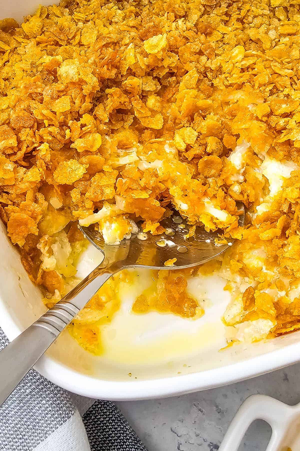 A serving spoon rests in a casserole dish  topped with a crunchy golden crust.