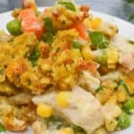 A delightful plate of chicken and stuffing casserole, featuring tender pieces of chicken mingled with vegetables like peas, carrots, and corn, all beneath a golden breadcrumb crust.