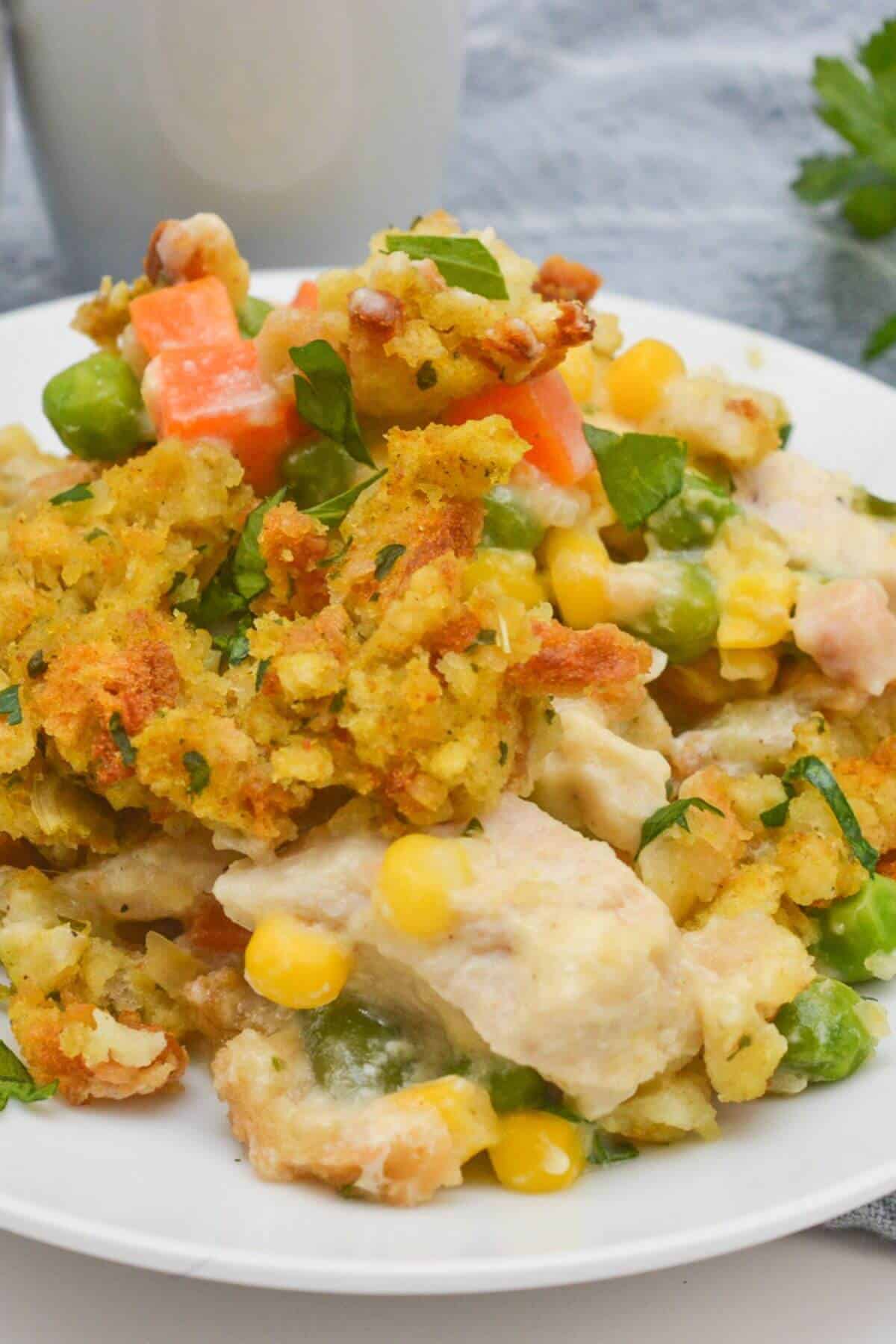 A delightful plate of chicken and stuffing casserole, featuring tender pieces of chicken mingled with vegetables like peas, carrots, and corn, all beneath a golden breadcrumb crust.