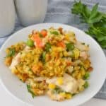 A delightful plate of chicken and stuffing casserole accompanied by mixed vegetables. Peas, carrots, and corn are garnished with parsley, all beautifully presented on a white dish next to two sleek white salt and pepper shakers.