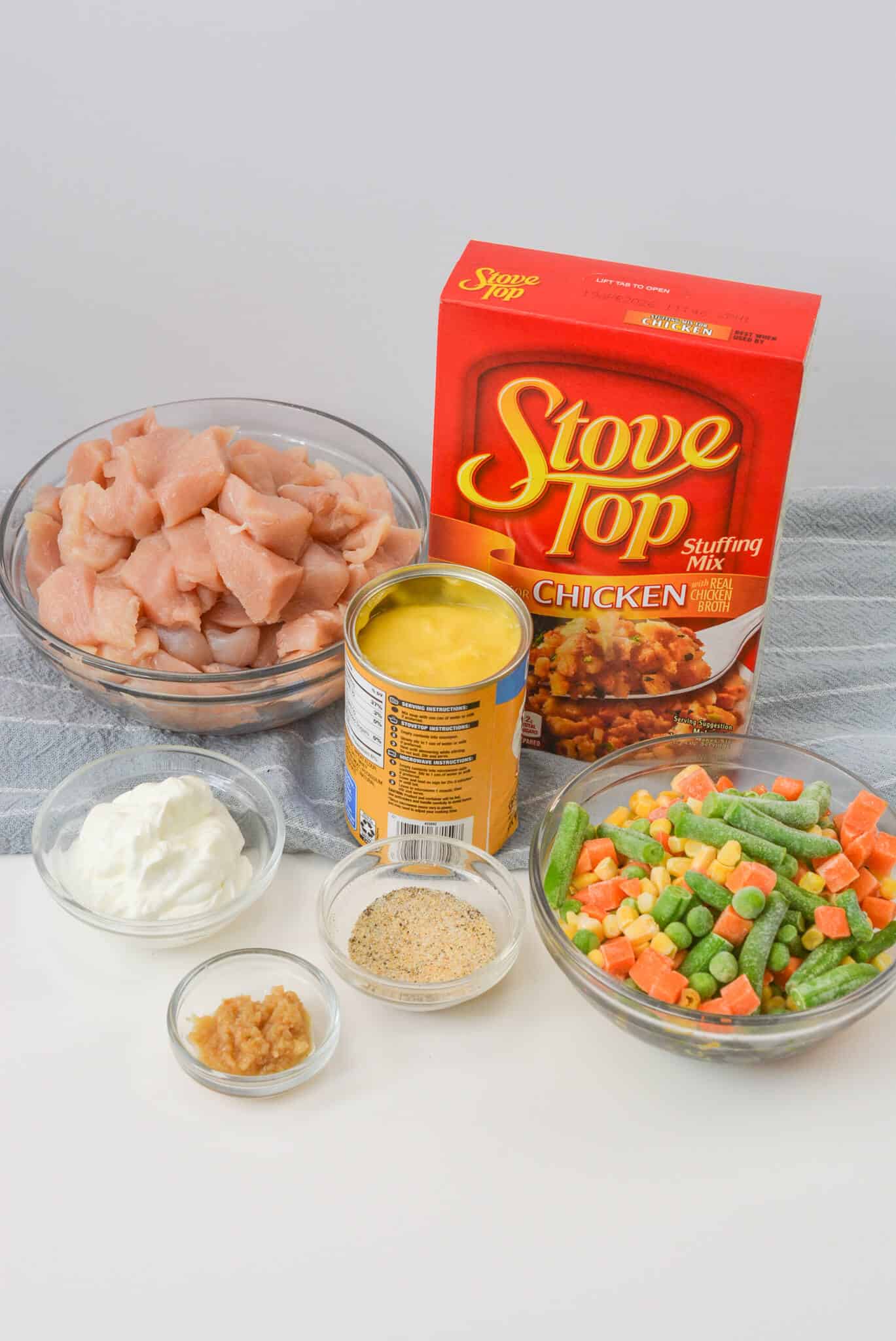 Ingredients for a the dinner including diced chicken, mixed vegetables, cream of chicken soup, stuffing mix, sour cream, garlic, and breadcrumbs, beautifully arranged on a counter.