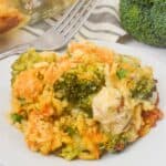 A serving of Chicken Broccoli Divan casserole on a white plate with a fork, next to fresh broccoli and a baking dish.