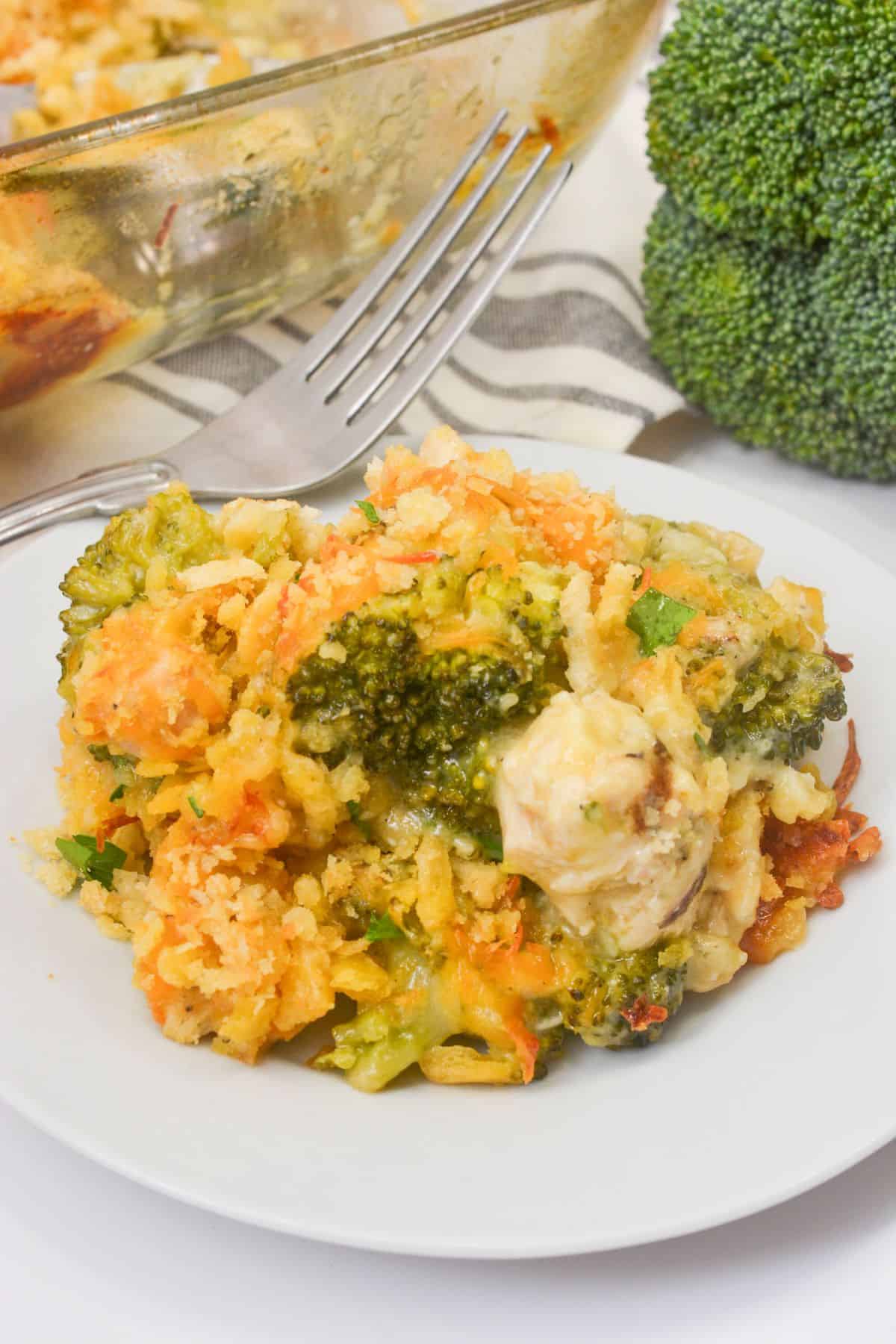 A serving of Chicken Broccoli Divan casserole on a white plate with a fork, next to fresh broccoli and a baking dish.