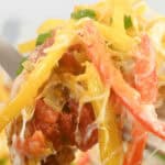 Close-up of a forkful of nachos topped with melted cheese, red and yellow bell peppers, tomatoes, and green garnish, reminiscent of flavors from a chicken fajita casserole.