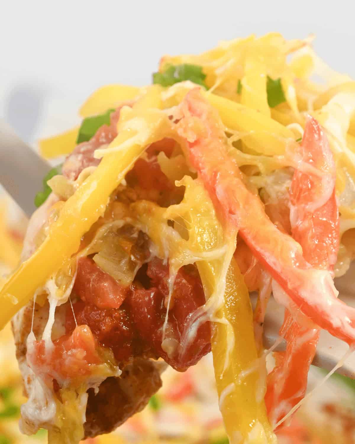 Close-up of a forkful of nachos topped with melted cheese, red and yellow bell peppers, tomatoes, and green garnish, reminiscent of flavors from a chicken fajita casserole.