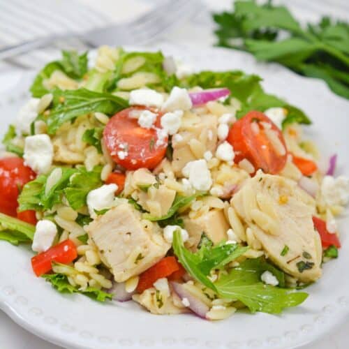 A plate with grilled chicken, cherry tomatoes, leafy greens, red onions, red peppers, and crumbled feta cheese.