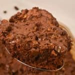 A close-up of a spoon holding the gooey, dessert above a tray of in the back.