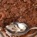 A close-up of a glass baking dish with a chocolate dump cake, partially scooped out, showing a serving spoon resting inside.