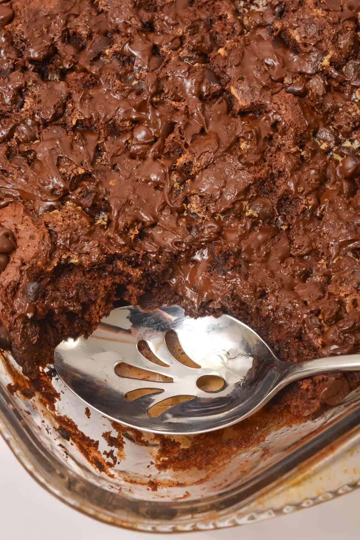 A close-up of a glass baking dish with a chocolate dump cake, partially scooped out, showing a serving spoon resting inside.