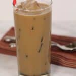 A tall glass of caramel iced coffee with a striped straw sits on a marble surface, accompanied by a folded napkin and spoon.