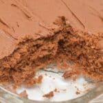 A Cocoa Mayonnaise Cake, rectangular with rich chocolate frosting and a missing large piece, sits temptingly in a glass baking dish.