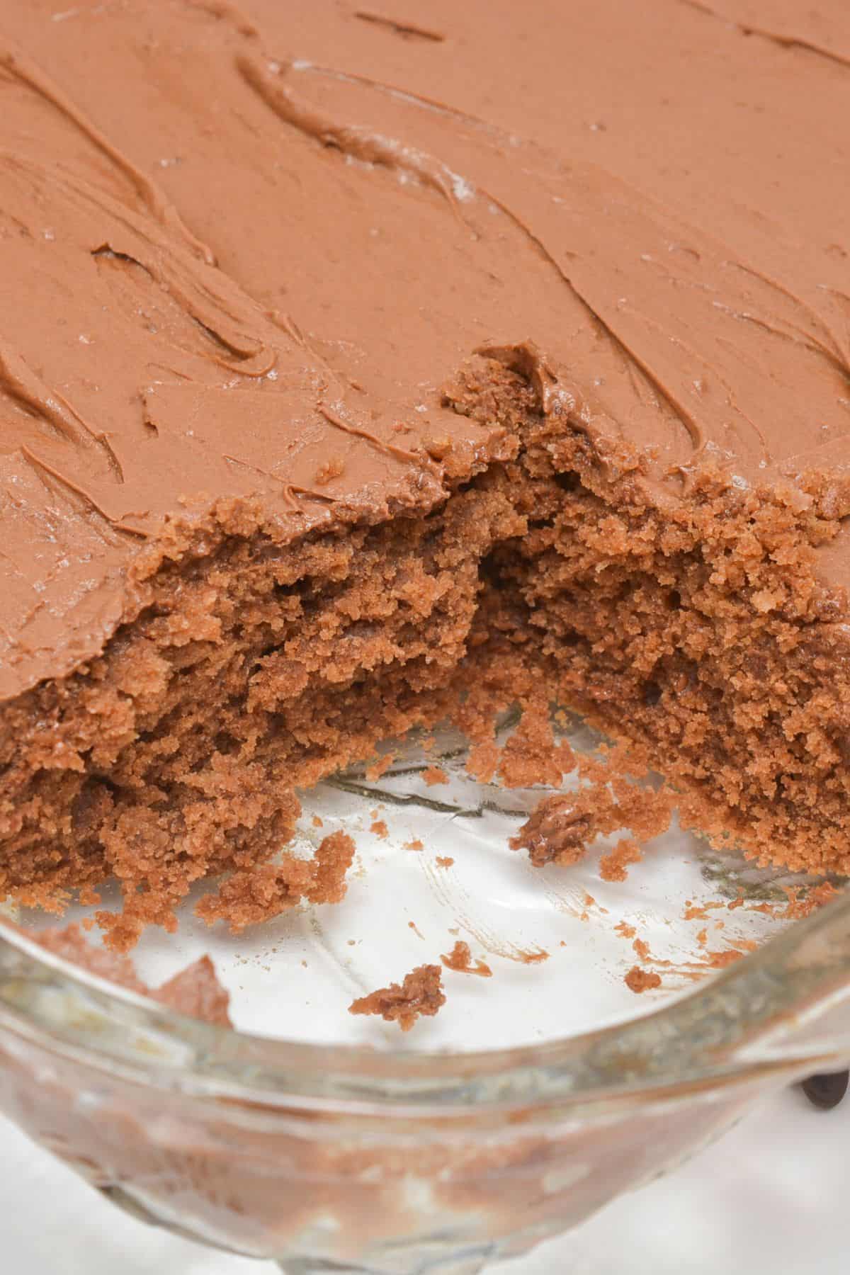 A rectangular with rich chocolate frosting and a missing large piece, sits temptingly in a glass baking dish.