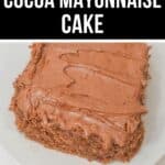 A slice of rich Cocoa Mayonnaise Cake with chocolate frosting sits on a white plate, shown from above.