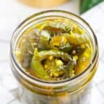 A glass jar filled with sliced Cowboy Candy jalapeños and visible seeds, all immersed in tangy brine.
