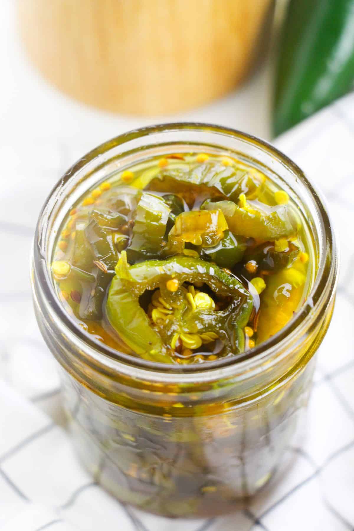 A glass jar filled with sliced Cowboy Candy jalapeños and visible seeds, all immersed in tangy brine.
