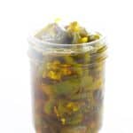 A glass jar filled with sliced jalapeños in brine, placed against a white background.